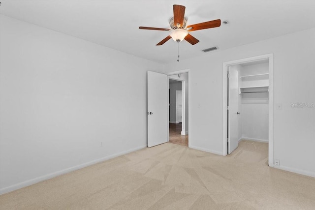 unfurnished bedroom featuring ceiling fan, light colored carpet, a closet, and a walk in closet