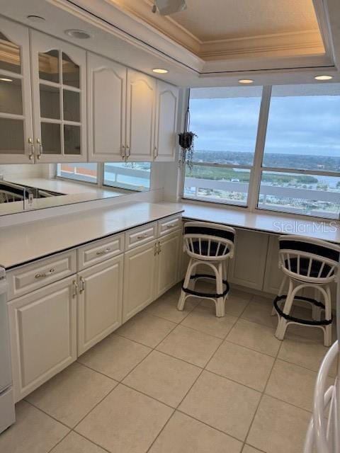 kitchen featuring ornamental molding, a tray ceiling, light tile patterned floors, and white cabinets