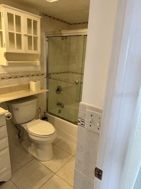 full bathroom featuring toilet, tile walls, vanity, enclosed tub / shower combo, and tile patterned flooring