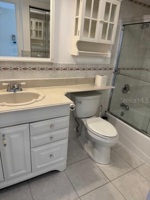 full bathroom featuring tile walls, shower / bath combination with glass door, tile patterned flooring, vanity, and toilet