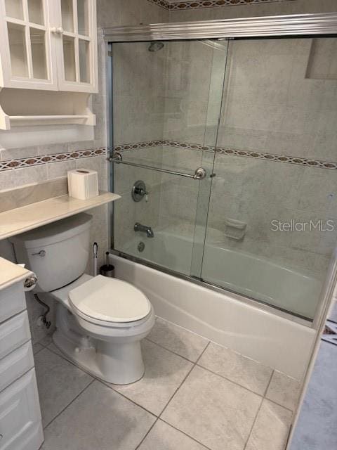 full bathroom with tile walls, shower / bath combination with glass door, vanity, toilet, and tile patterned floors