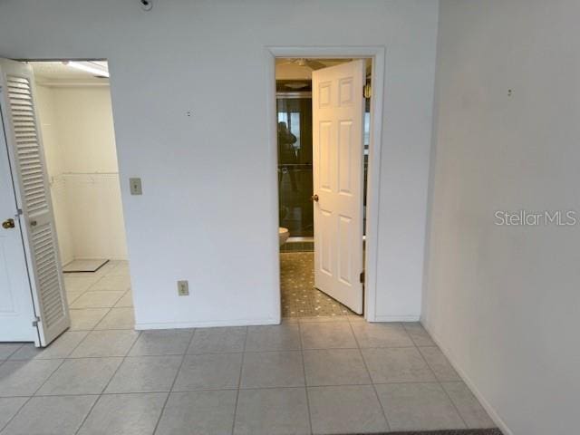 unfurnished bedroom with light tile patterned floors, a spacious closet, a closet, and ensuite bathroom