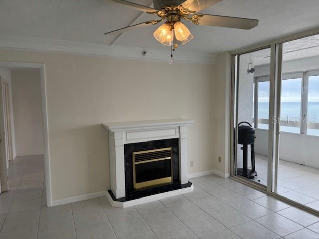 unfurnished living room with ornamental molding, light tile patterned flooring, ceiling fan, and a fireplace