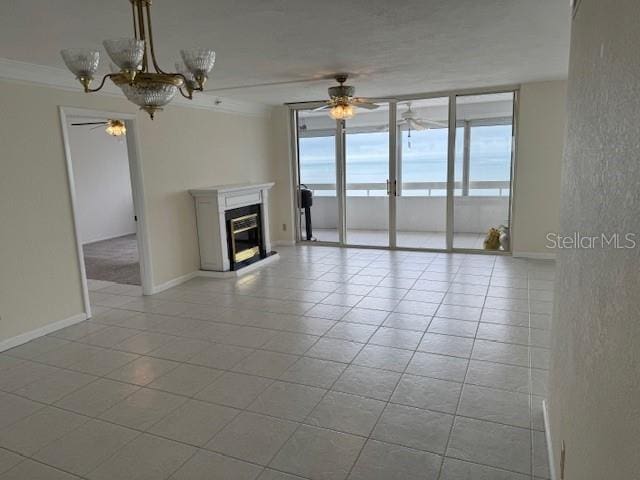 unfurnished living room featuring crown molding, ceiling fan with notable chandelier, a wall of windows, and light tile patterned floors