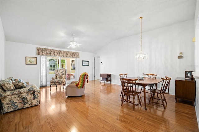 dining space with ceiling fan with notable chandelier, wood-type flooring, and vaulted ceiling