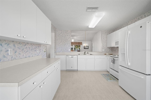 kitchen featuring pendant lighting, white cabinetry, sink, white appliances, and a textured ceiling