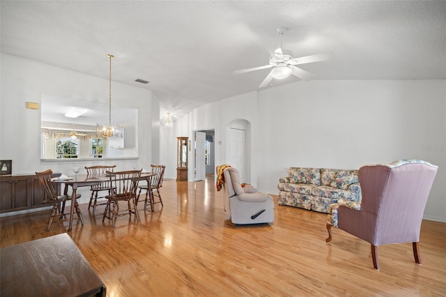 living room featuring lofted ceiling, ceiling fan with notable chandelier, light hardwood / wood-style flooring, and a textured ceiling