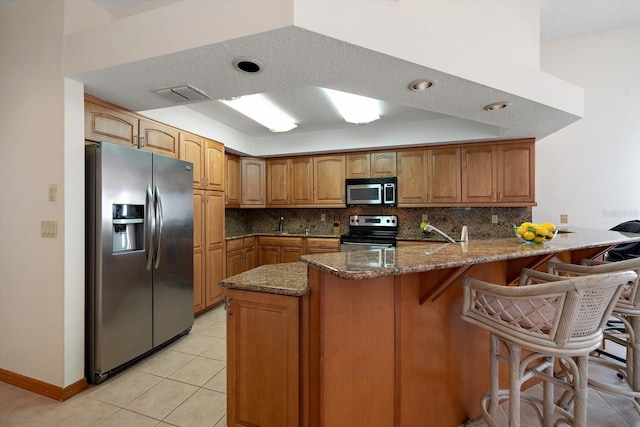 kitchen featuring appliances with stainless steel finishes, dark stone countertops, a kitchen breakfast bar, tasteful backsplash, and kitchen peninsula