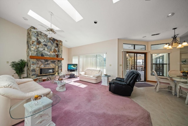 living room with light tile patterned flooring, a stone fireplace, a skylight, high vaulted ceiling, and ceiling fan with notable chandelier