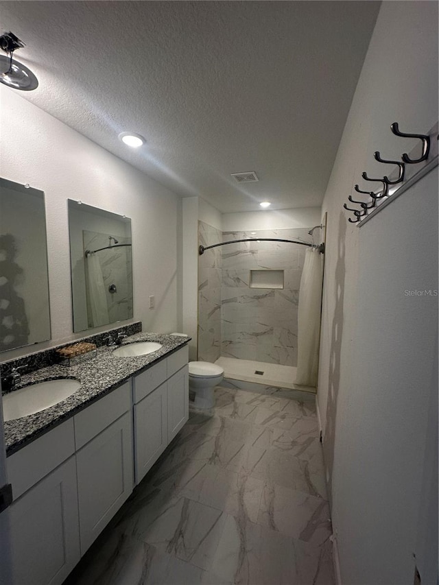 bathroom featuring a tile shower, vanity, toilet, and a textured ceiling