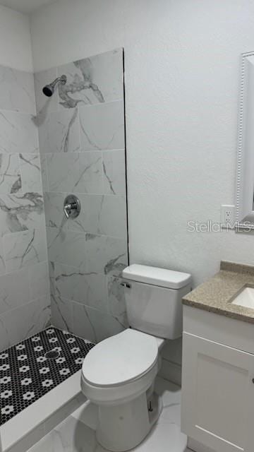 bathroom featuring vanity, a tile shower, and toilet