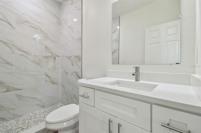 bathroom with a tile shower, vanity, and toilet