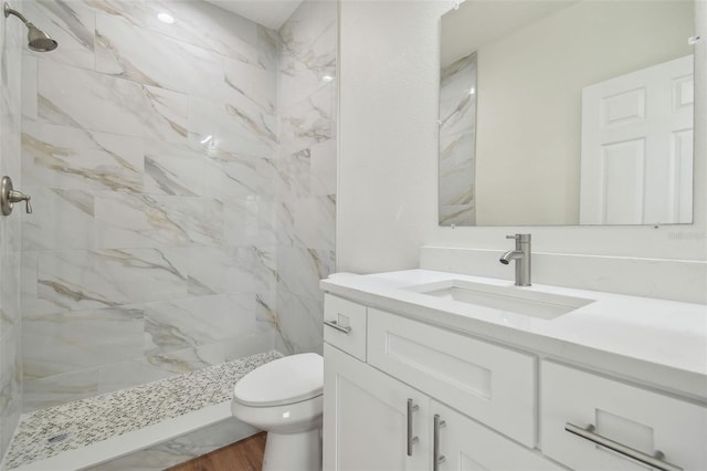 bathroom featuring a tile shower, vanity, and toilet