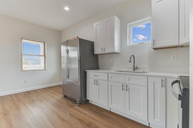 kitchen with sink, light hardwood / wood-style flooring, stainless steel fridge, white cabinets, and stove