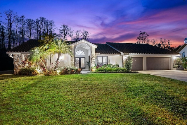 view of front facade with concrete driveway, stucco siding, an attached garage, french doors, and a front yard