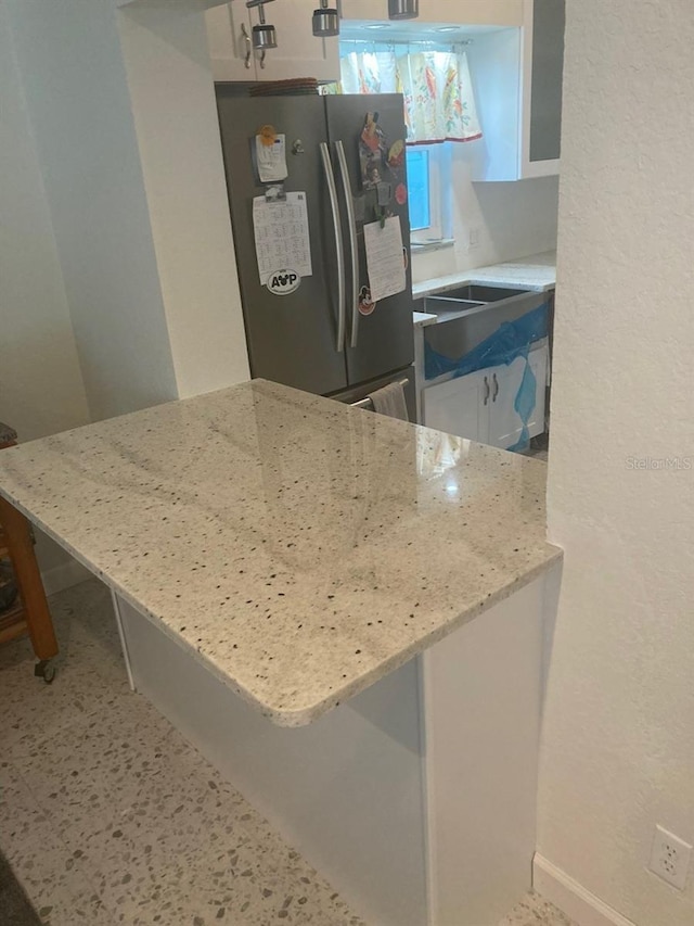 kitchen with white cabinets, stainless steel fridge, a kitchen bar, kitchen peninsula, and light stone countertops