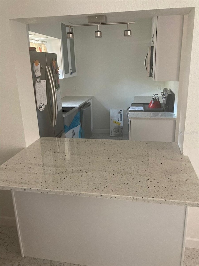 kitchen with stainless steel appliances, white cabinetry, light stone countertops, and kitchen peninsula