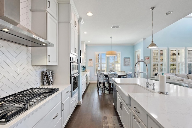 kitchen featuring sink, white cabinetry, decorative light fixtures, appliances with stainless steel finishes, and wall chimney range hood