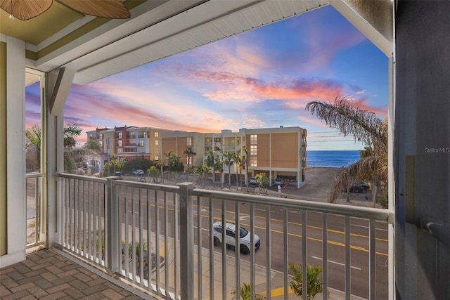 balcony at dusk with a water view and ceiling fan