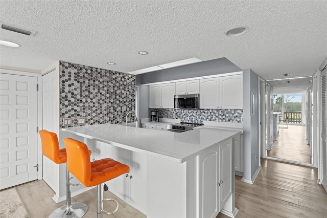 kitchen featuring a breakfast bar, light hardwood / wood-style flooring, kitchen peninsula, stainless steel appliances, and white cabinets