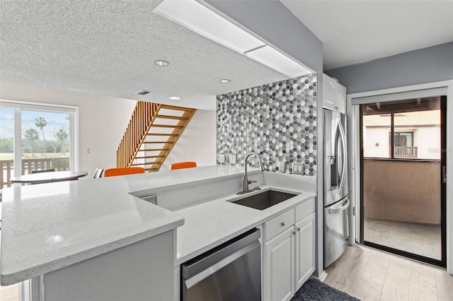 kitchen featuring sink, white cabinetry, light stone counters, appliances with stainless steel finishes, and kitchen peninsula