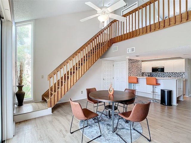 dining area with ceiling fan, a towering ceiling, and light wood-type flooring