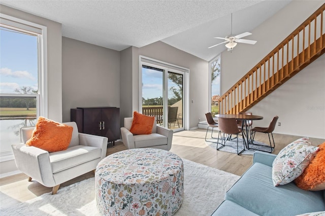 living room featuring ceiling fan, lofted ceiling, a textured ceiling, and light hardwood / wood-style floors