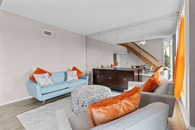 living room with ceiling fan, a textured ceiling, and light wood-type flooring