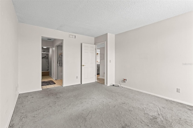 unfurnished bedroom featuring ensuite bathroom, light colored carpet, and a textured ceiling