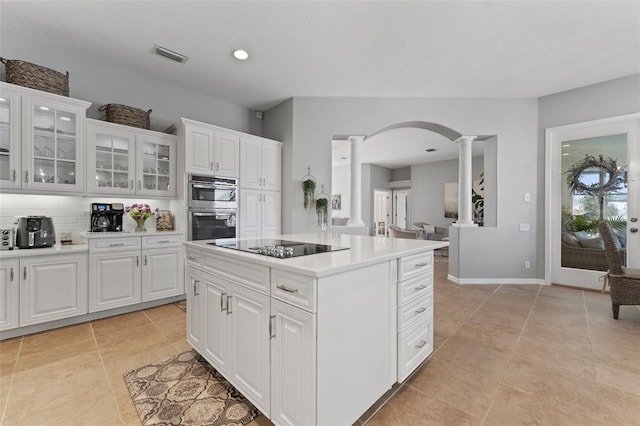 kitchen featuring double oven, decorative columns, black electric stovetop, white cabinets, and a kitchen island