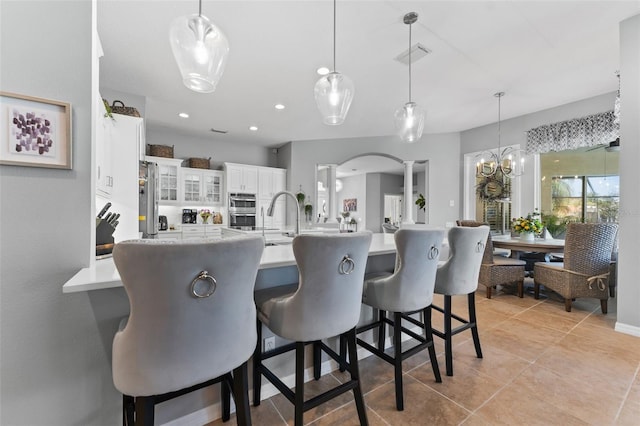 kitchen with a kitchen bar, stainless steel fridge, decorative columns, and hanging light fixtures