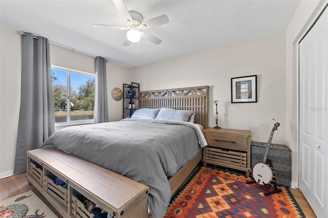 bedroom featuring ceiling fan, a textured ceiling, light wood-type flooring, and a closet