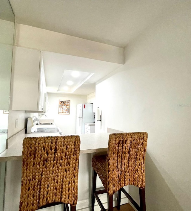 kitchen featuring a breakfast bar area, light countertops, stove, freestanding refrigerator, and a peninsula