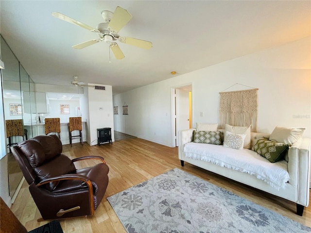 living area with a ceiling fan, visible vents, and wood finished floors