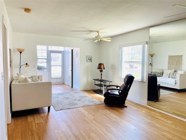 living area with baseboards, a ceiling fan, and light wood-style floors