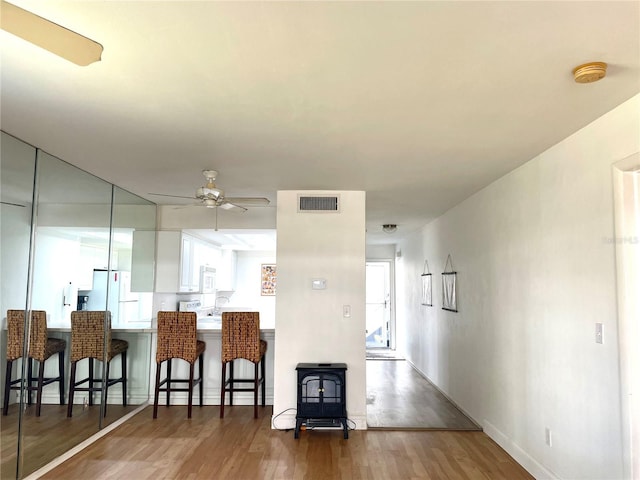 kitchen with a ceiling fan, a breakfast bar, wood finished floors, freestanding refrigerator, and a wood stove