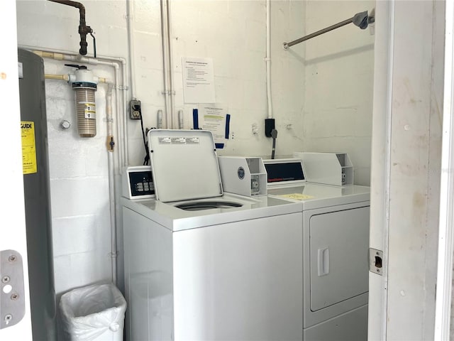 common laundry area with concrete block wall, water heater, and washer and clothes dryer