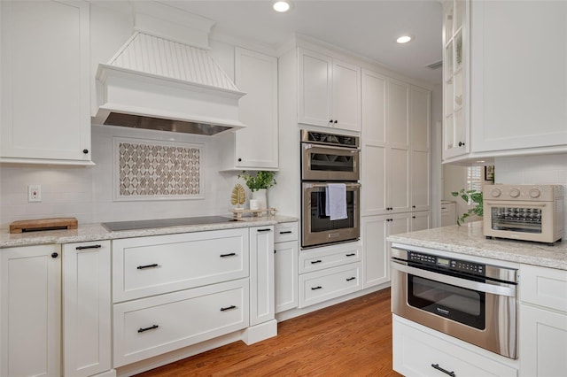 kitchen featuring custom exhaust hood, white cabinetry, black electric cooktop, stainless steel double oven, and backsplash