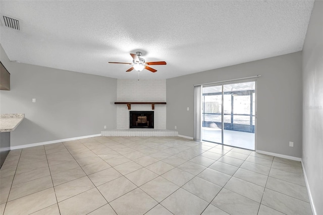 unfurnished living room with ceiling fan, light tile patterned floors, a brick fireplace, and a textured ceiling