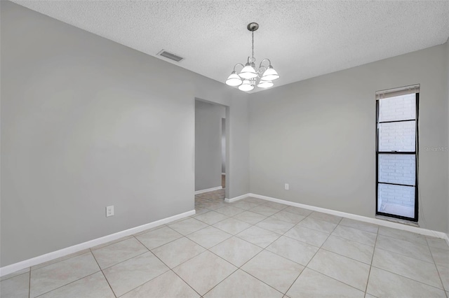 empty room with light tile patterned flooring, a textured ceiling, and a notable chandelier