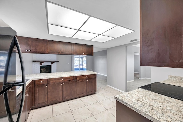 kitchen featuring black refrigerator, light tile patterned floors, light stone counters, kitchen peninsula, and dark brown cabinets