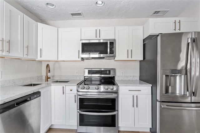 kitchen featuring light stone counters, stainless steel appliances, a textured ceiling, and white cabinets