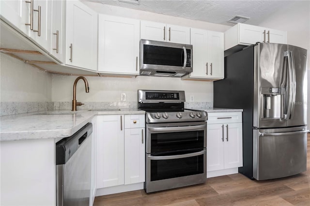 kitchen with a textured ceiling, dark wood-type flooring, stainless steel appliances, and white cabinets