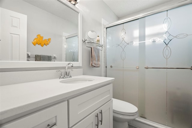 bathroom with vanity, a textured ceiling, a shower with shower door, and toilet