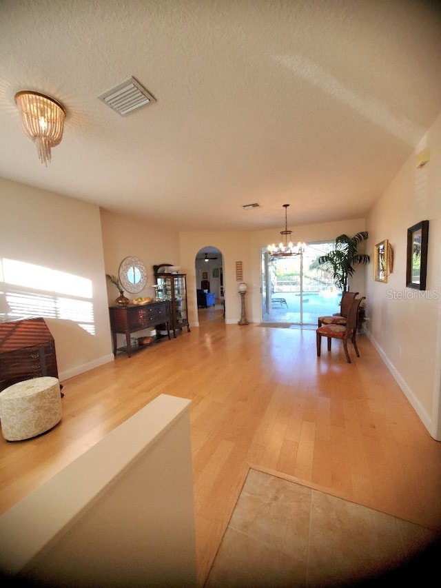 unfurnished living room with visible vents, arched walkways, a textured ceiling, light wood-style floors, and a notable chandelier