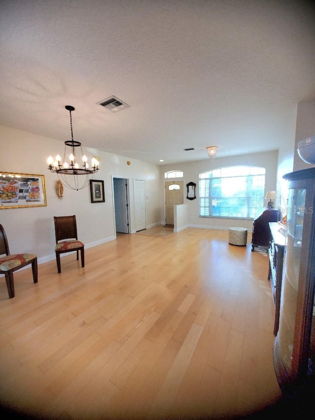 living room with visible vents, an inviting chandelier, a textured ceiling, light wood-type flooring, and baseboards