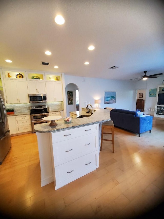 kitchen with arched walkways, a kitchen island with sink, stainless steel appliances, a sink, and visible vents