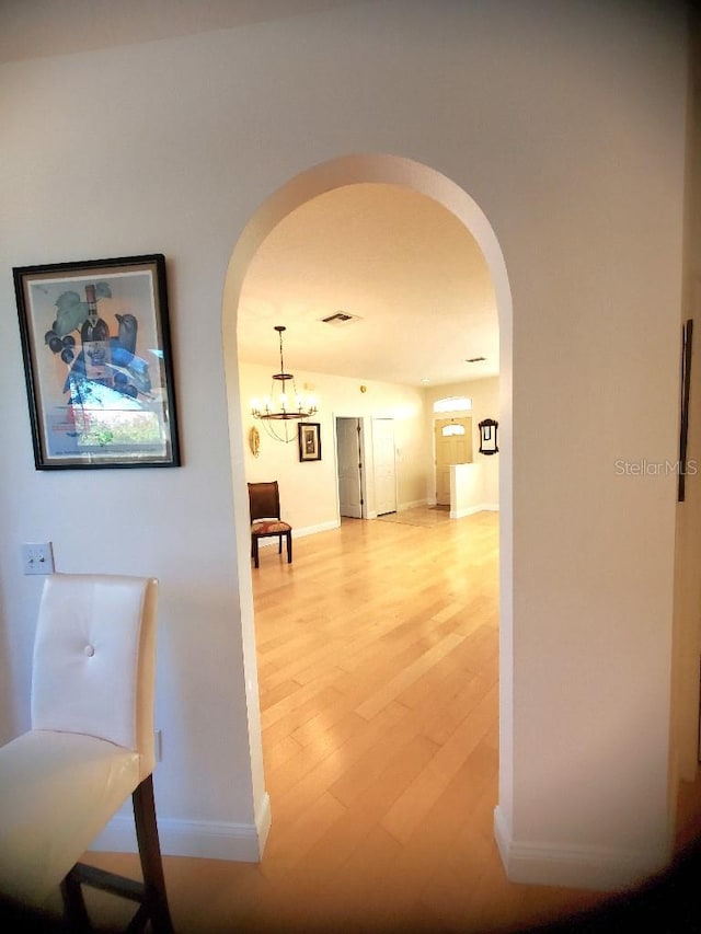 hall with arched walkways, baseboards, visible vents, and light wood-style floors