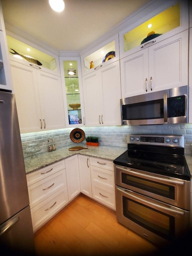 kitchen with stainless steel appliances, light stone countertops, white cabinets, and tasteful backsplash