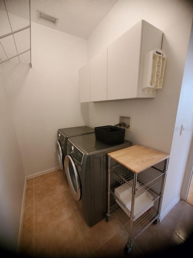 clothes washing area with light tile patterned floors, visible vents, baseboards, cabinet space, and washer and clothes dryer